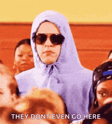 a person wearing a hoodie and sunglasses is standing in front of a crowd of people .