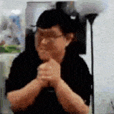 a man in a black shirt and glasses is praying with his hands folded .