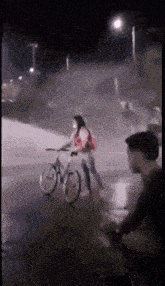 a woman is riding a bike down a street at night while a man watches .