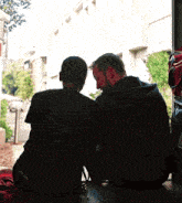 two men are looking out of a window and one has a backpack on his back