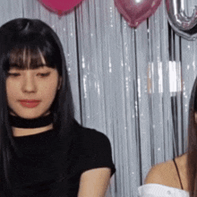 two women are standing in front of a curtain with pink balloons .