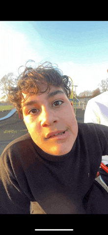 a young man with curly hair is making a funny face in front of a playground