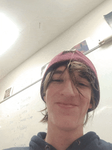a boy wearing a beanie stands in front of a white board with the names charlotte dorian luca and emma-hoe written