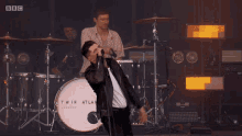 a man singing into a microphone in front of a drum that says twin atlantic