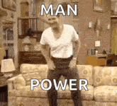 a man is dancing in front of a couch in a living room with the words man power written on it .