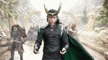 loki is wearing a helmet and holding a sword while standing in front of a group of people .