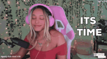 a woman wearing pink headphones is sitting in front of a microphone with the words its time above her