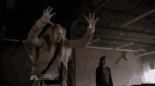 a woman in a trench coat holds her hands up in the air in front of a sign that says " truth be told "