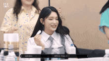 a girl in a white shirt and tie is smiling while sitting at a table with bottles of water