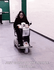 a woman is riding a scooter in a hallway and says `` just going to the temple session '' .