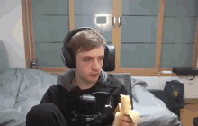 a young man wearing headphones is sitting on a bed eating a banana .