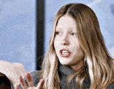 a woman wearing a grey sweater has her hand up in the air