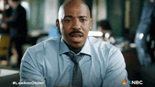 a man in a blue shirt and tie is sitting in front of a nbc sign