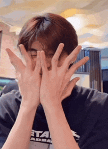 a man covering his face with his hands while wearing a black shirt that says star wars