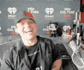 a man is laughing in front of a wall that says pop culture weekly