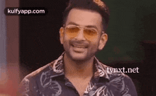 a man wearing sunglasses and a black shirt is smiling and looking at the camera .