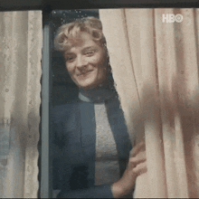 a woman is looking out of a window with a hbo logo on the bottom right corner .