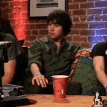 a man in a green shirt is sitting at a table with a cup on it .