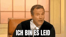 a man in a suit and tie is sitting in a chair with the words ich bin es leid written on his face .