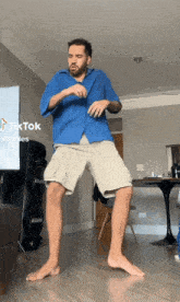 a man in a blue shirt and khaki shorts is dancing in a living room with a tik tok watermark