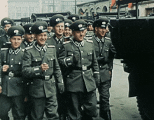 a group of soldiers are marching down a street and one of them is wearing a hat with the letter a on it