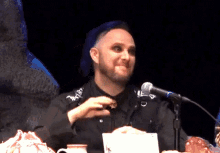 a man with purple hair is sitting at a table with a microphone in front of him