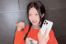 a girl in a red shirt is holding a white cell phone