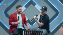 two men singing into microphones in front of a rtve sign