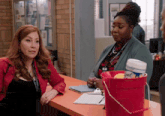two women sitting at a counter with a red bucket of cleaning supplies