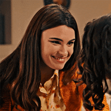 a woman wearing a polka dot shirt and an orange jacket smiles