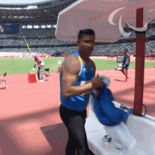 a man in a blue tank top is standing in front of a stadium
