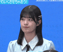 a girl in a blue shirt with a black tie looks at the camera with a blue background