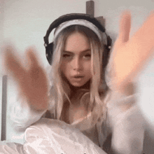 a woman wearing headphones is sitting on a bed with her hands up .