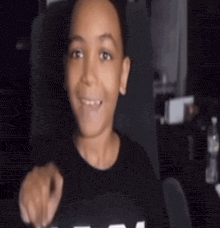 a young boy is sitting in a chair and smiling while pointing at the camera .