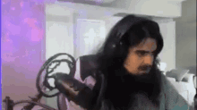 a man with long black hair is wearing headphones and holding a microphone in a room .