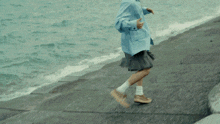 a person in a blue jacket is running on a beach near the water
