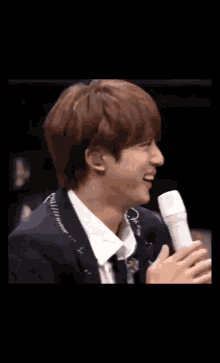 a man in a suit and tie is singing into a microphone while laughing .