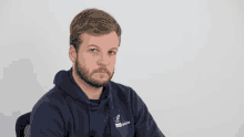a man with a beard wears a blue hoodie with the word mano on it