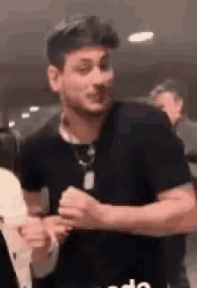 a man wearing a black shirt and a necklace is standing in a crowd of people .