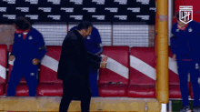 a man in a black jacket is dancing in a locker room with powerade advertisements on the wall behind him
