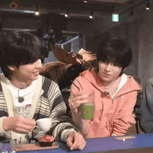 two boys are sitting at a table drinking green tea and eating cupcakes