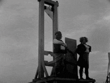 a black and white photo of two men standing in front of a guillotine ..