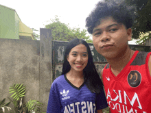 a man and a woman are posing for a picture with the man wearing a red jersey that says asim