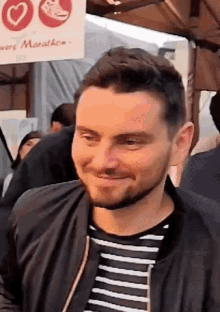 a man wearing a striped shirt and a black jacket is smiling in front of a sign that says marathon