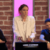a woman in a white jacket stands in front of a laink & damdam sign