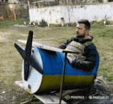 a man sits in a blue and yellow barrel with a propeller on it