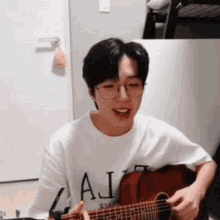 a young man wearing glasses is playing a guitar and singing .