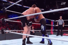 two men are wrestling in a wrestling ring with a referee in the background .