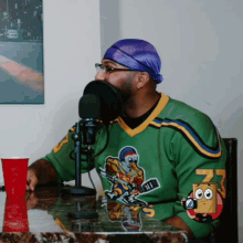 a man wearing a green jersey with a hockey player on it sits in front of a microphone