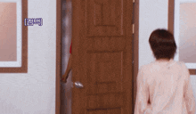a woman in a pink shirt is standing in front of a wooden door with a foreign language written on it
